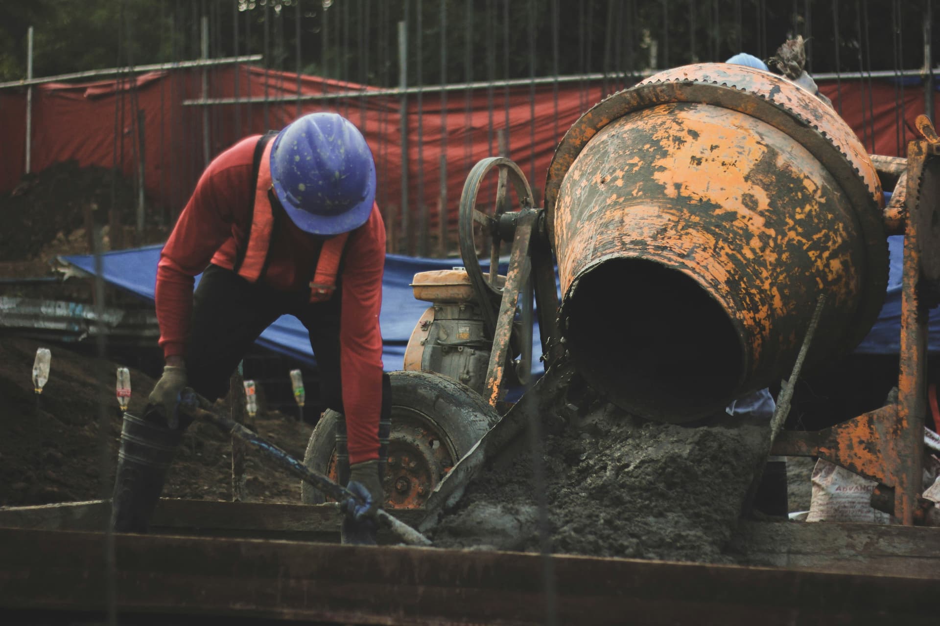 A worker placing concrete beside a mixer and formwork